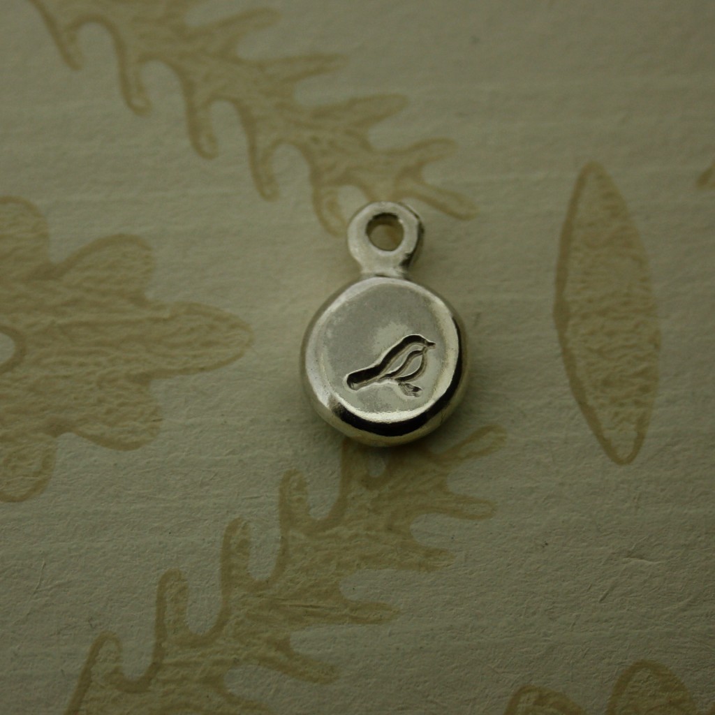 Round silver pebble hand stamped with a bird symbol