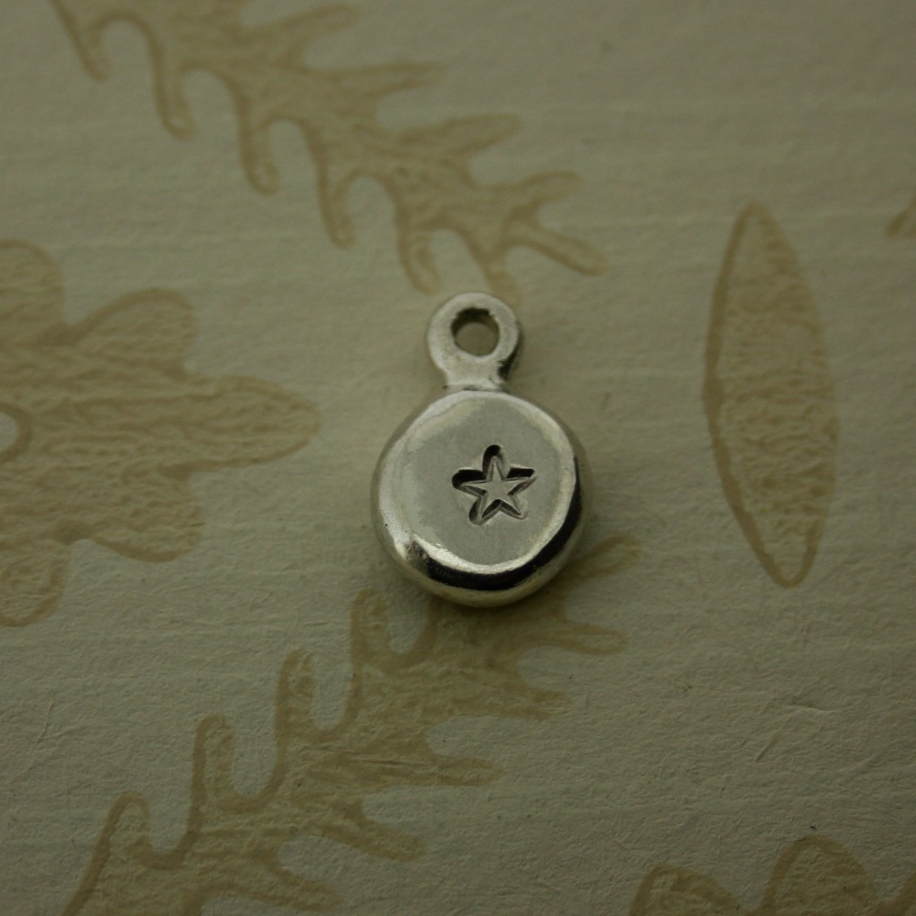 silver pebble charm hand stamped with a star shape