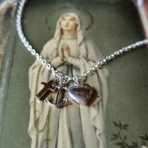 small silver heart and anchor strung on a silver chain with a small gold cross